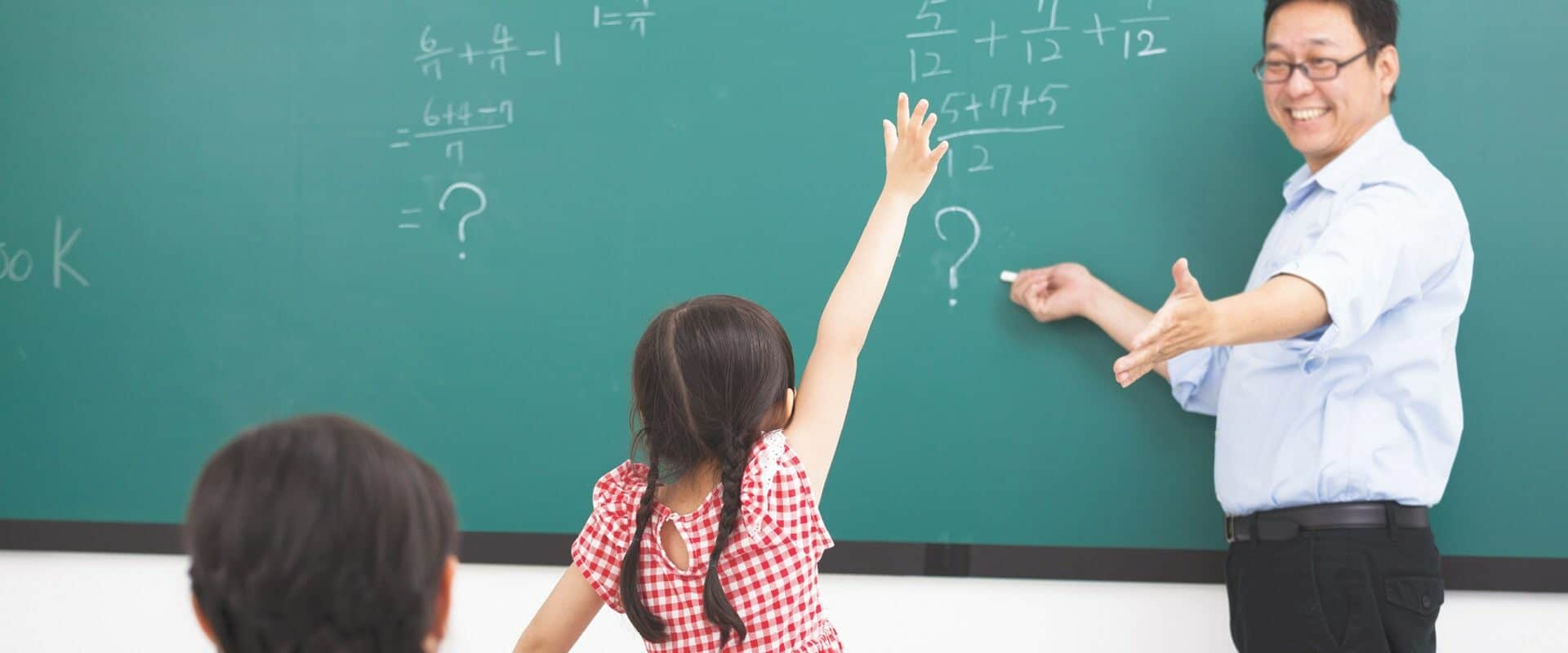 Young girl standing up with a raised hand during math lesson and male teacher calling calling on her (Tom Wang/Shutterstock.com) - EDUCATIONAL AUDIOLOGY | Scope of Practice for Educational Audiology Article