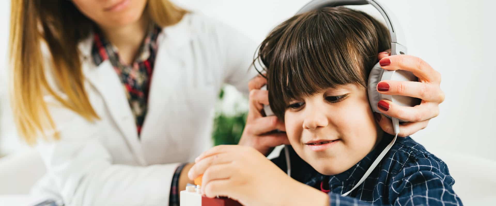 Female audiologist testing young boy hearing while he is playing with blocks (Microgen/Shutterstock.com)