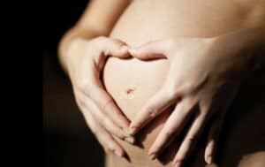 Close-up of a pregnant woman's hands displaying a heart over her belly