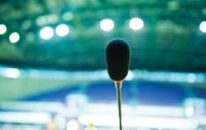 Close-up photo of public speaking microphone in front of blurred room of people - PUBLIC RELATIONS | Media Training: Do I Need This? Article