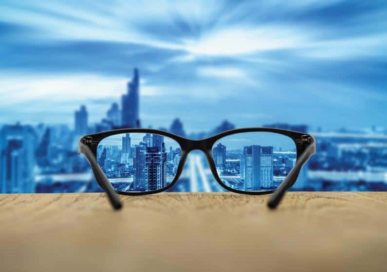 Close-up of glasses on a window ledge with the glasses showing clear view of city and the city in the background is blurry