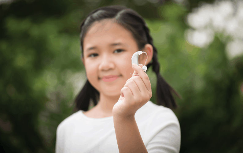 Out-of-focus image of an asian girl holding up a hearing aid