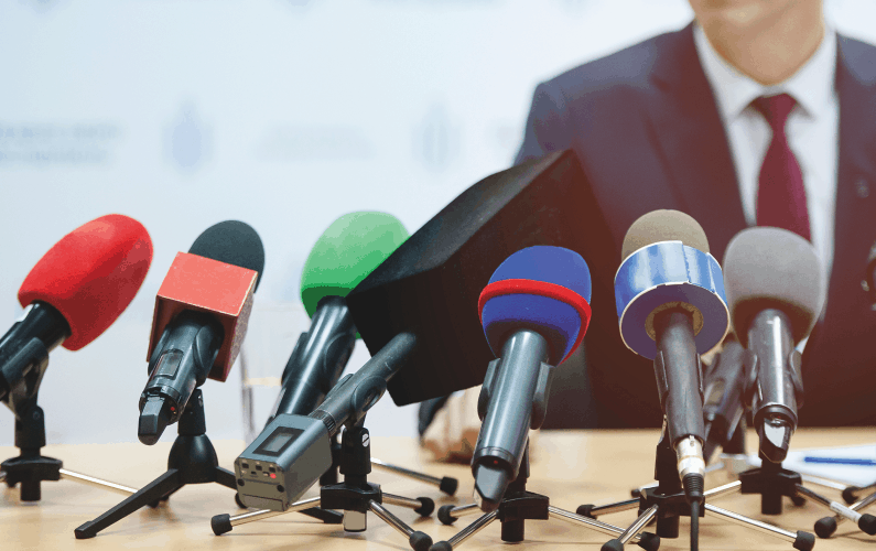 photo of man in front of microphones for news briefing - PUBLIC RELATIONS | Getting Media Coverage Is Only Part of the Equation Article