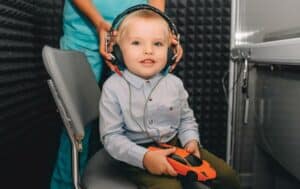 Photo of toddler having headphones placed on head by audiologist to get hearing test