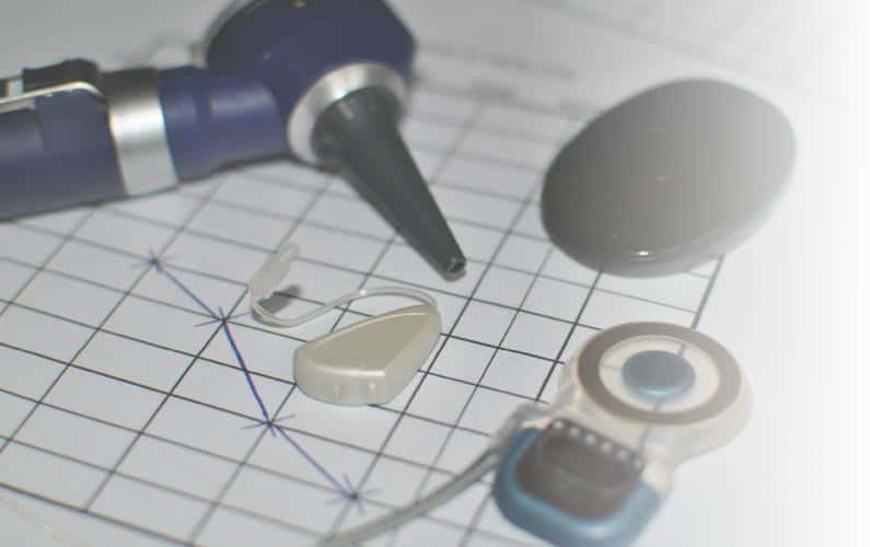 Photo of otoscope, hearing exam form, hearing aid, and cochlear implant