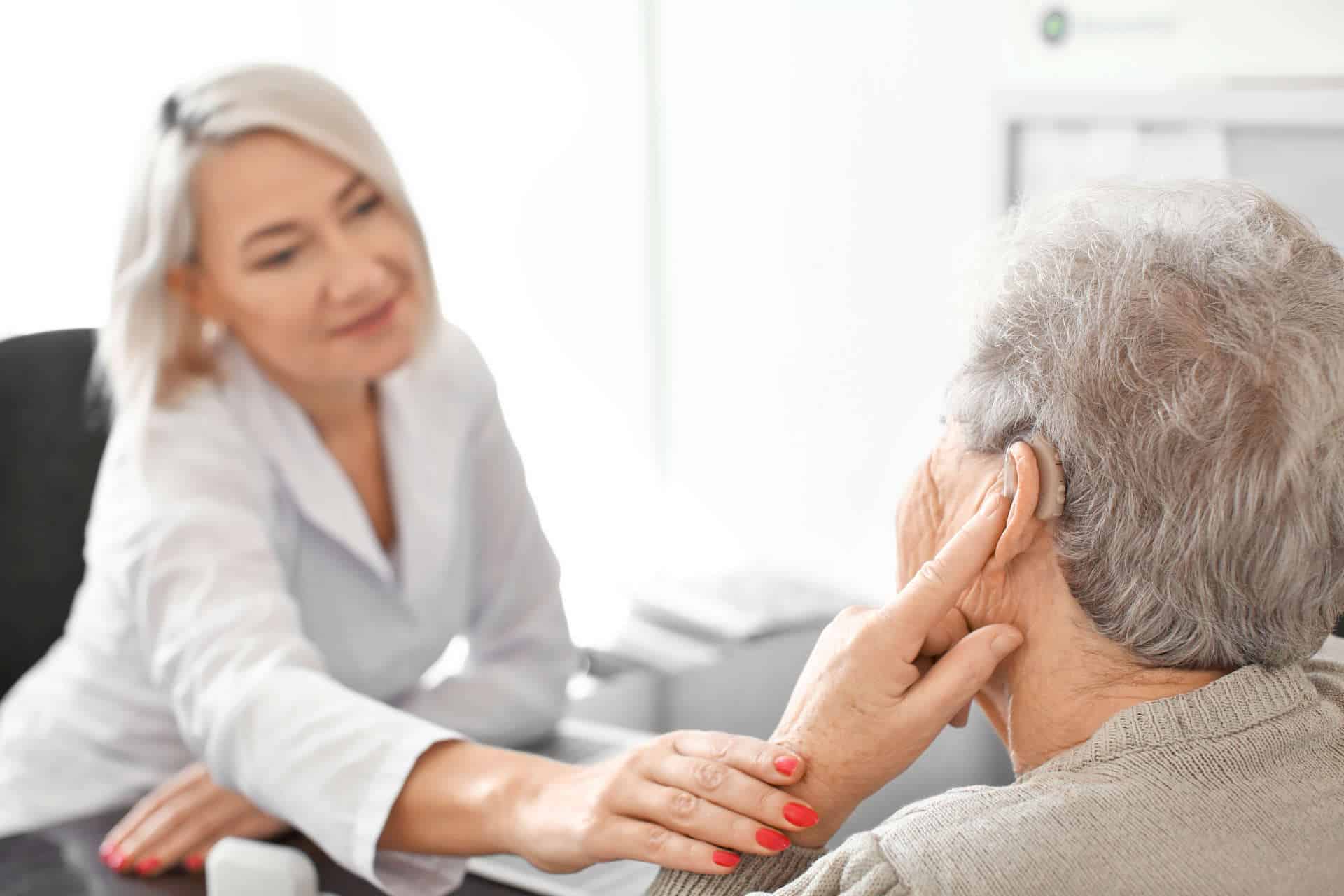 senior-woman-adjusting-hearing-aid-doctor-s-office senior-woman-adjusting-hearing-aid-doctor-s-office