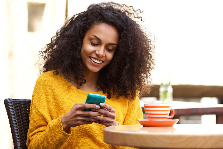 Close up portrait of beautiful young african american woman reading text message on mobile phone at coffee shop