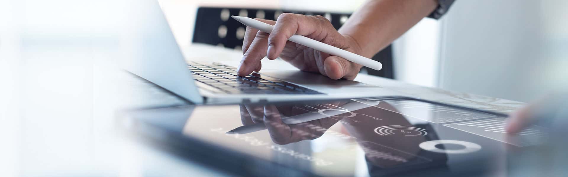 Businessman working on laptop, using mobile phone at modern office, analyzing business document with financial graph, market report on digital tablet, business data analysis concept. Shutterstock Image.