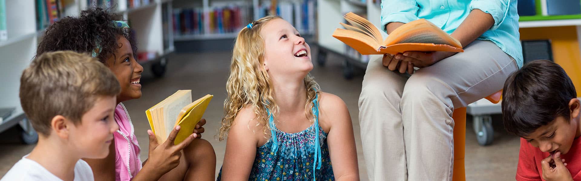 Low section of female teacher with smiling children reading books in library. Shutterstock Image.
