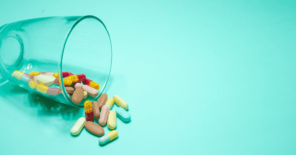 Drugs spilling from glass cup, over isolated green background.