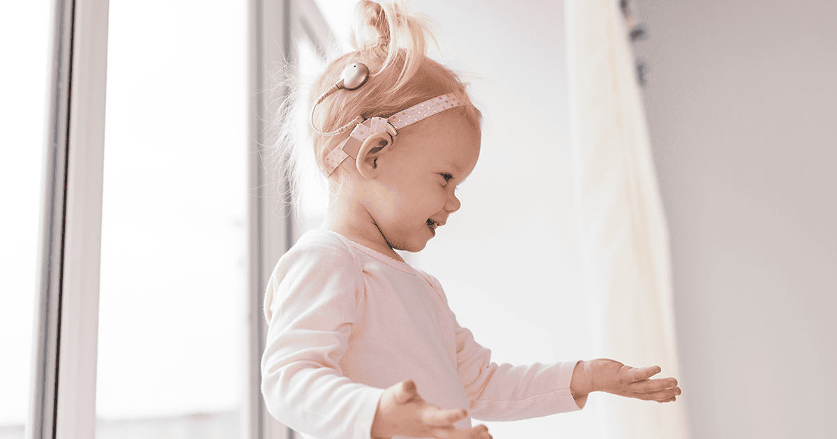 Funny baby with cochlear implant sitting at home and eating. Hear aid and medicine innovating technology and diversity concept - How Well Do Parents and Professionals Know Their Child’s Cochlear Implant?